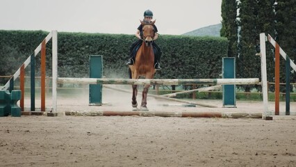 Young boy on horse jumping over obstacles during training in paddock, horse riding lessons.