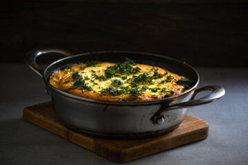 Rustic omelet with potatoes and herbs in a metal pan on the kitchen table.