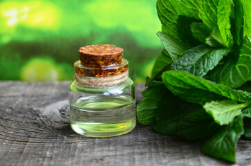 Peppermint essential oil in a glass bottle with fresh green mint leaves on old wooden table for spa,aromatherapy,homeopathy and bodycare.