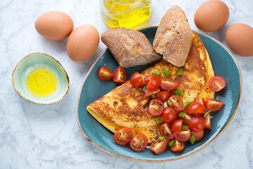 Omelette served with fresh cherry tomatoes and brown bread, high angle view on a light-grey marble background, horizontal shot
