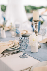 Long dinner tables covered with white cloth, served with porcelain and blue glasses and rich decorated with flowers 