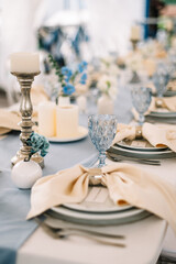 Long dinner tables covered with white cloth, served with porcelain and blue glasses and rich decorated with flowers 