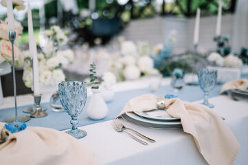 Outdoor banquet and modern design for wedding ceremony in summer. Linen tablecloth, candles, flowers and accessories, glasses and plates on table for guests with chairs, flat lay, nobody