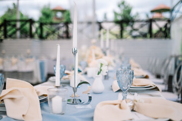 Outdoor banquet and modern design for wedding ceremony in summer. Linen tablecloth, candles, flowers and accessories, glasses and plates on table for guests with chairs, flat lay, nobody