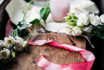 Drops on reading glasses next to white flowers with pink ribbon
