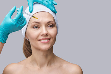 Face needle injection. Young woman cosmetology procedure. Doctor hand in green glove. Pretty female...