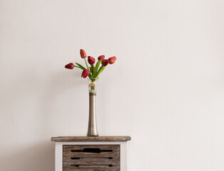 Slim vase with colorful red tulips on vintage wooden table against warm wall on cozy room