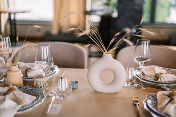Wedding table setting in rustic style with feathers. beige tablecloths and white plates. on a background of a white pompous hall top view
