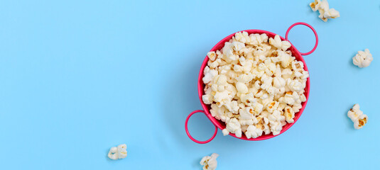 Fresh popcorn in a pink bowl on a blue background. Banner. Top view with copy space. The concept of snacks for cinemas.
