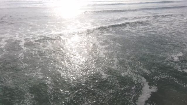 aerial footage of the rippling vast blue ocean water with majestic waves braking and rolling into the beach at Oxnard State Beach Park in Oxnard California USA