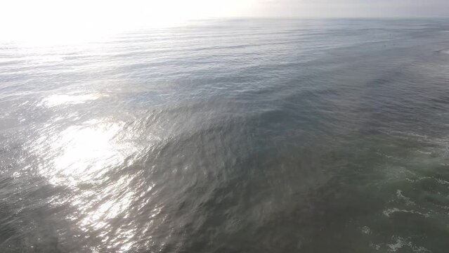aerial footage of the rippling vast blue ocean water with majestic waves braking and rolling into the beach at Oxnard State Beach Park in Oxnard California USA
