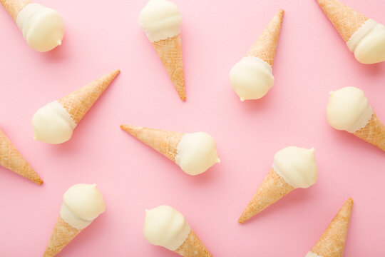 Waffle cones of white vanilla ice cream on light pink table background. Pastel color. Closeup. Cold sweet snack in summer. Food pattern. Top down view.