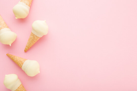 Waffle cones of white vanilla ice cream on light pink table background. Pastel color. Closeup. Cold sweet snack in summer. Empty place for text. Top down view.