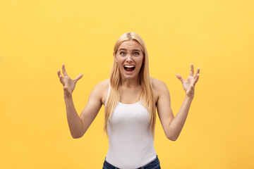 Portrait of an angry irritated woman with hands raised shouting at camera isolated on yellow...