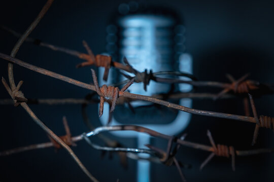Microphone behind barbed wire as a symbol of discrimination, free speech crisis, political persecution and repression. Selective focus on barbed wire. Horizontal image.