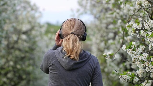 Happy woman with headphones listening music and dancing outdoors in spring nature. Enjoyment and happiness of carefree life