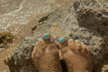 Women's feet with a bright turquoise polish on a stone by the sea