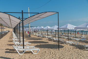 Beautiful empty beach with sun umbrellas and sunbeds. Perfect summer vacation destination. Straw sunshades and sunbeds on the empty beach with blue sea on background
