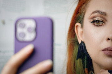 Red-haired girl takes selfie on front camera of smartphone. Female blogger runs a blog about fashion and makeup. Woman with Gothic-style jewelry with proud expression on her face. Witch aesthetic.