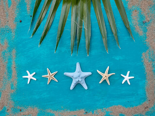 Fototapeta na wymiar Green palm leaf and several dry starfish on aquamarine background