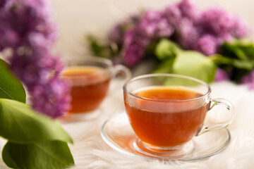 A cup of green tea against the background of a spring bouquet of lilacs on a white texture wood. Romantic composition with books and candles. spring tea drink. Place to copy. Romantic concept.