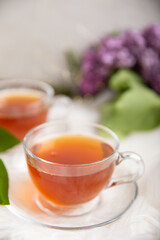 A cup of green tea against the background of a spring bouquet of lilacs on a white texture wood. Romantic composition with books and candles. spring tea drink. Place to copy. Romantic concept.