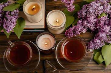 Obraz na płótnie Canvas A cup of green tea against the background of a spring bouquet of lilacs on a brown texture wood. Romantic composition with books and candles. spring tea drink. Place to copy. Romantic concept.