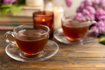 A cup of green tea against the background of a spring bouquet of lilacs on a brown texture wood. Romantic composition with books and candles. spring tea drink. Place to copy. Romantic concept.