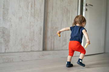 Back view full length of one small toddler caucasian boy or girl waking going out while holding toys in hands copy space childhood development and growing up concept © Miljan Živković