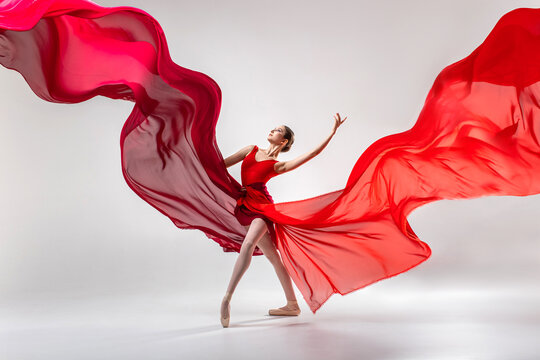 Fototapeta Ballerina in red leotard dancing in white studio room with red clothes waving around