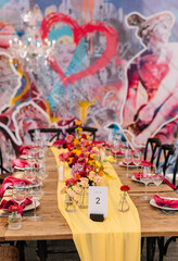 festive tables and chairs, tables decorated with compositions of flowers and candles. Yellow tablecloth. Pink napkin On the tables are glasses, plates and cutlery