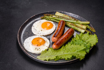 A delicious nourishing breakfast with fried eggs, sausages, asparagus, tomatoes, avocado, spices and herbs