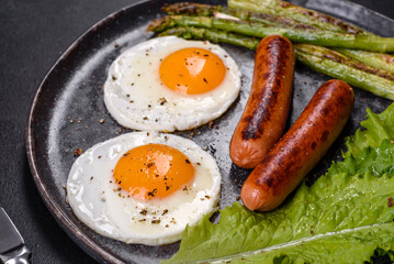 A delicious nourishing breakfast with fried eggs, sausages, asparagus, tomatoes, avocado, spices and herbs