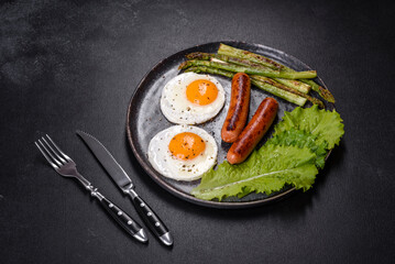 A delicious nourishing breakfast with fried eggs, sausages, asparagus, tomatoes, avocado, spices and herbs