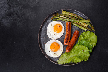 A delicious nourishing breakfast with fried eggs, sausages, asparagus, tomatoes, avocado, spices and herbs
