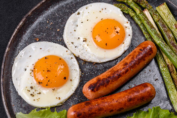 A delicious nourishing breakfast with fried eggs, sausages, asparagus, tomatoes, avocado, spices and herbs