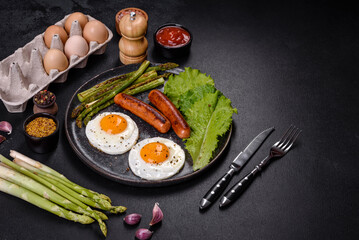A delicious nourishing breakfast with fried eggs, sausages, asparagus, tomatoes, avocado, spices and herbs