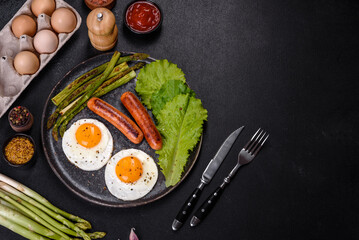 A delicious nourishing breakfast with fried eggs, sausages, asparagus, tomatoes, avocado, spices and herbs