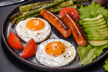 A delicious nourishing breakfast with fried eggs, sausages, asparagus, tomatoes, avocado, spices and herbs