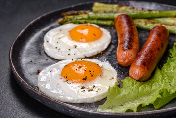 A delicious nourishing breakfast with fried eggs, sausages, asparagus, tomatoes, avocado, spices and herbs