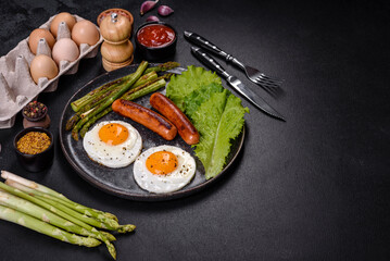 A delicious nourishing breakfast with fried eggs, sausages, asparagus, tomatoes, avocado, spices and herbs