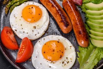 A delicious nourishing breakfast with fried eggs, sausages, asparagus, tomatoes, avocado, spices and herbs
