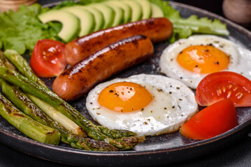A delicious nourishing breakfast with fried eggs, sausages, asparagus, tomatoes, avocado, spices and herbs