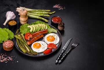 A delicious nourishing breakfast with fried eggs, sausages, asparagus, tomatoes, avocado, spices and herbs