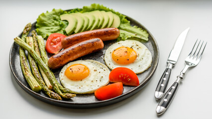 A delicious nourishing breakfast with fried eggs, sausages, asparagus, tomatoes, avocado, spices and herbs