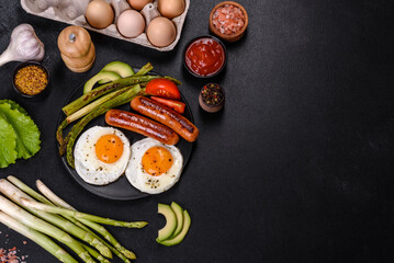 A delicious nourishing breakfast with fried eggs, sausages, asparagus, tomatoes, avocado, spices and herbs