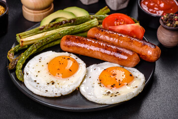 A delicious nourishing breakfast with fried eggs, sausages, asparagus, tomatoes, avocado, spices and herbs