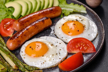 A delicious nourishing breakfast with fried eggs, sausages, asparagus, tomatoes, avocado, spices and herbs