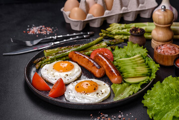 A delicious nourishing breakfast with fried eggs, sausages, asparagus, tomatoes, avocado, spices and herbs