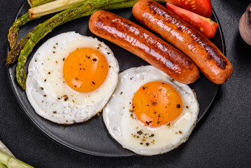 A delicious nourishing breakfast with fried eggs, sausages, asparagus, tomatoes, avocado, spices and herbs